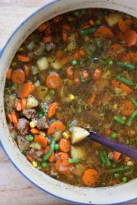a large pot of beef vegetable soup with carrots, potatoes, green beans, peas, and corn
