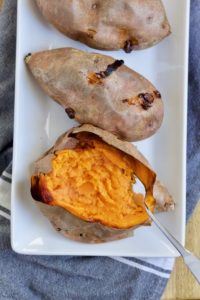 a tray of baked sweet potatoes with one cut open to reveal tender orange goodness