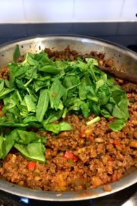 taco meat filling in the pan with a pile of fresh spinach waiting to be stirred in