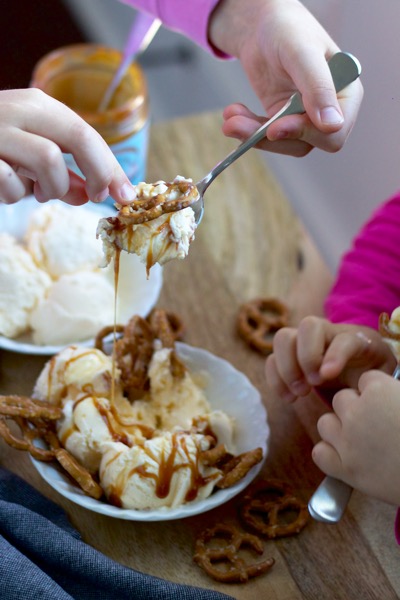 My helpers eating a huge bite of a sundae with dripping salted caramel and a crunchy pretzel