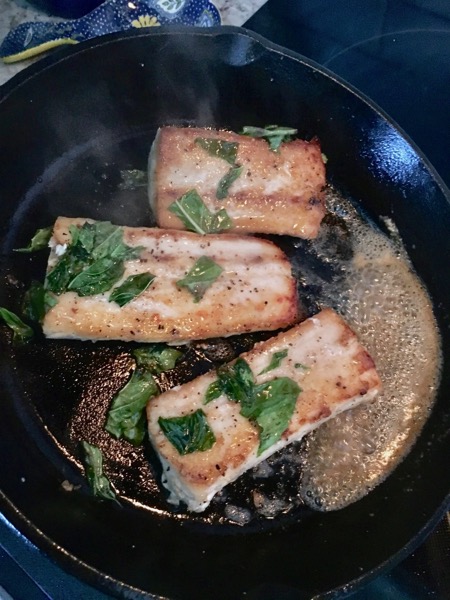 tilting the cast iron skillet and basting mahi-mahi fillets with melted butter