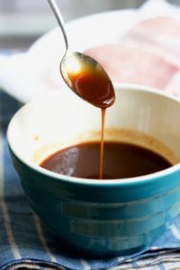 a spoon drizzling a thick, dark stream of honey bbq sauce into a bowl