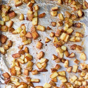 a foil-lined sheet pan with life-changing super crispy roasted potatoes scattered on it
