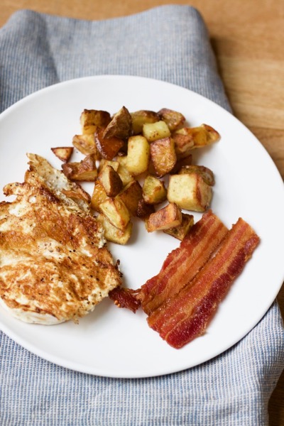 a plate with life-changing super crispy roasted potatoes, a fried egg, and bacon
