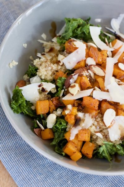 a bowl with kale, quinoa, roasted butternut squash with onions, parmesan cheese, sliced almonds, and balsamic drizzle